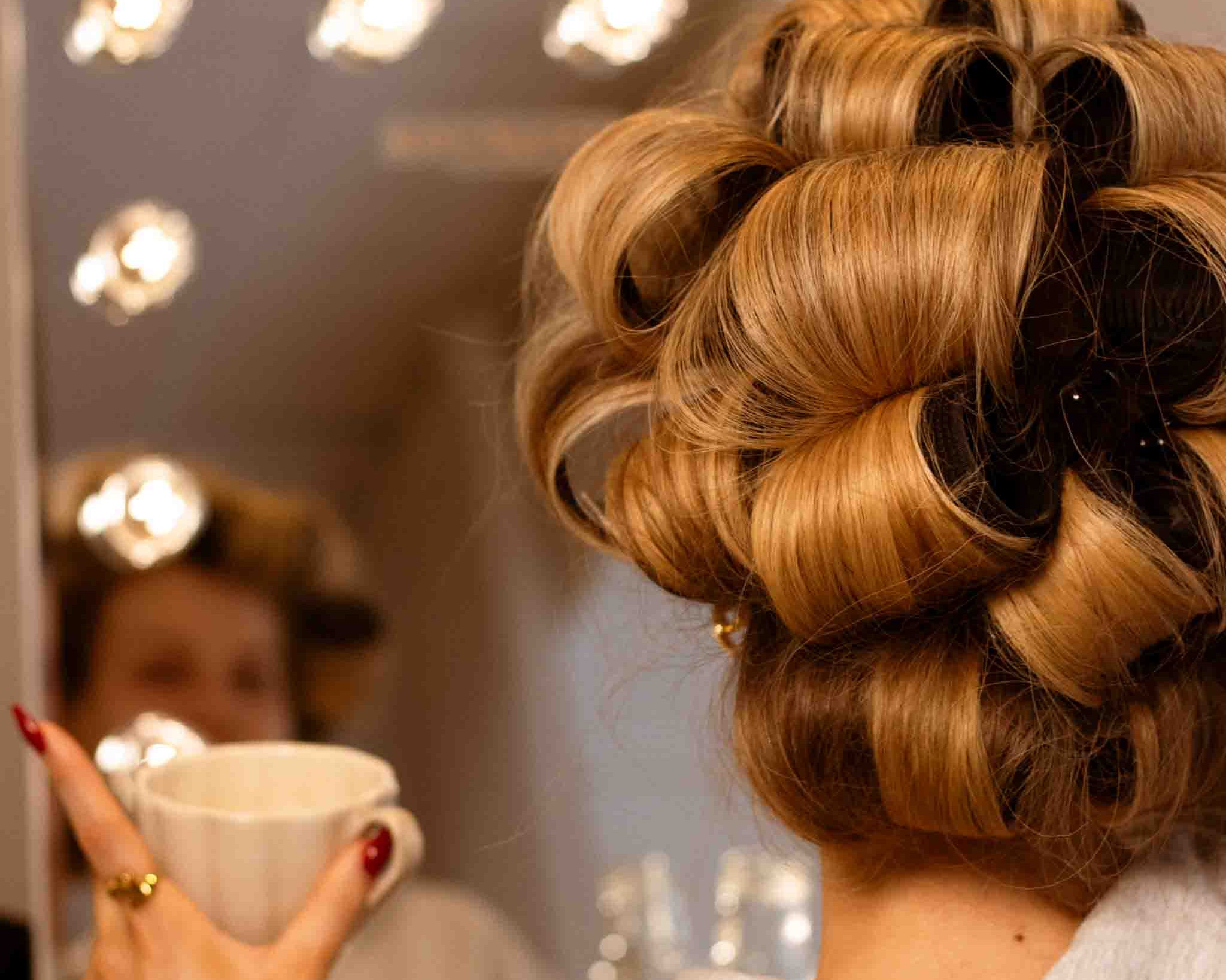Kvinna med uppsatt hår i stora lockar med hårklämmor framför spegeln – förberedelse för hållbara glansiga lockar med Your Steel Clips