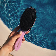 Your Hair Brush – Lavender Large från Molimenti, hålls i en hand med ljus manikyr vid kanten av en solbelyst pool. Den lila hårborsten med svart borsthuvud fångas i naturligt ljus, med blått vatten i bakgrunden som skapar en somrig och fräsch känsla.