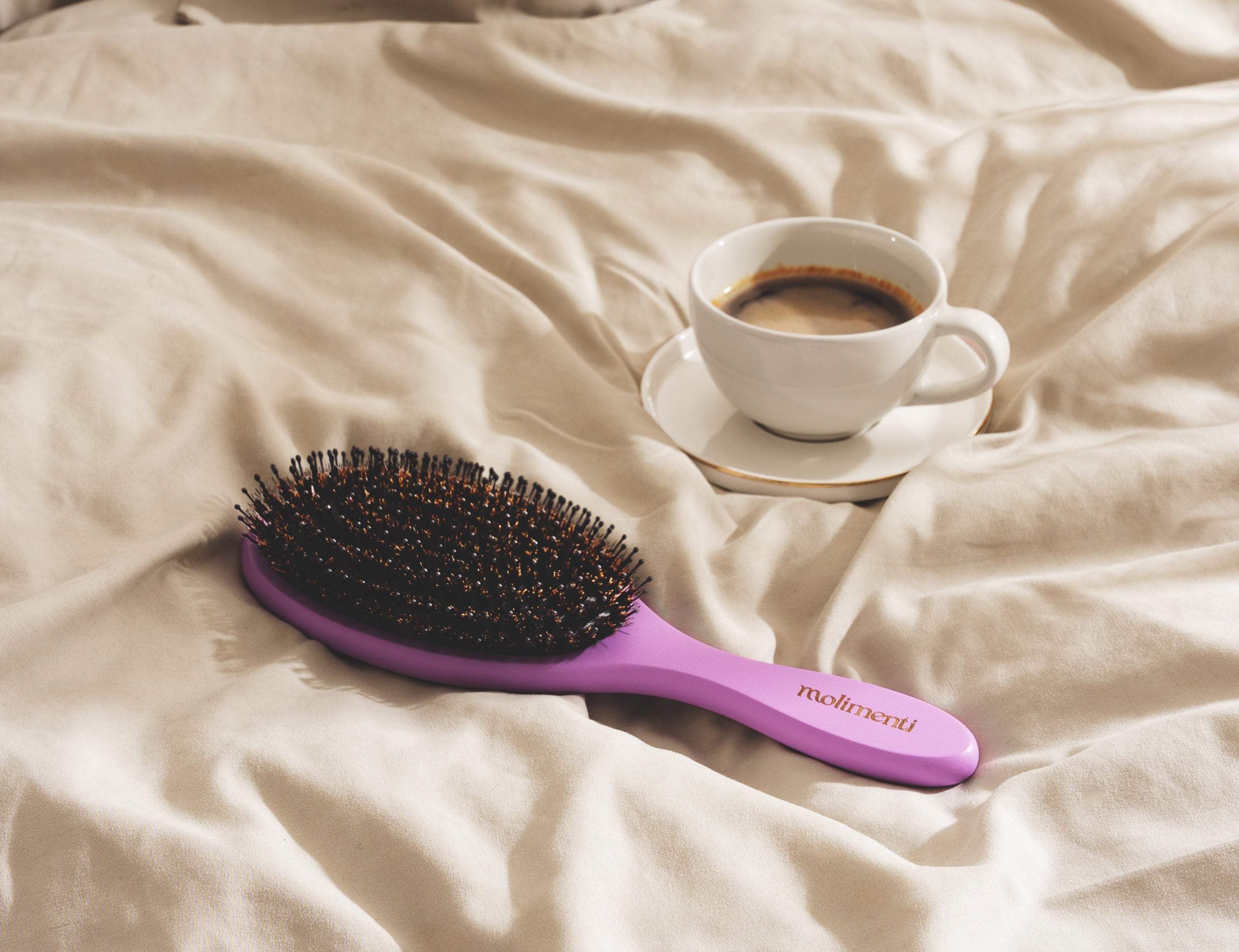 Närbild på hårborste med en kaffekopp på sängen.