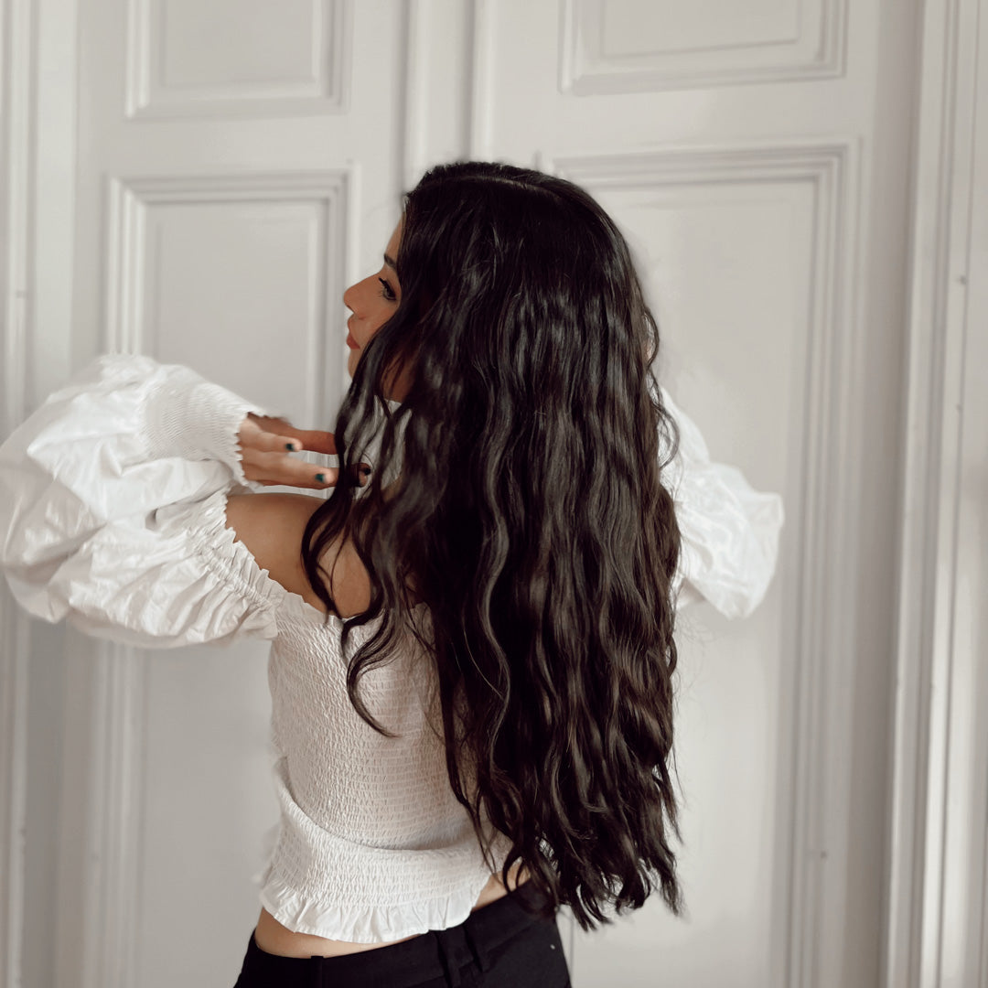Your Curl Wand - från Molimenti. Modell med mörkt hår fångas i rörelse när hon slänger med håret bakifrån, efter styling med Your Curl Wand från Molimenti. De mjuka, glansiga lockarna rör sig naturligt och visar upp ett livfullt och professionellt resultat.